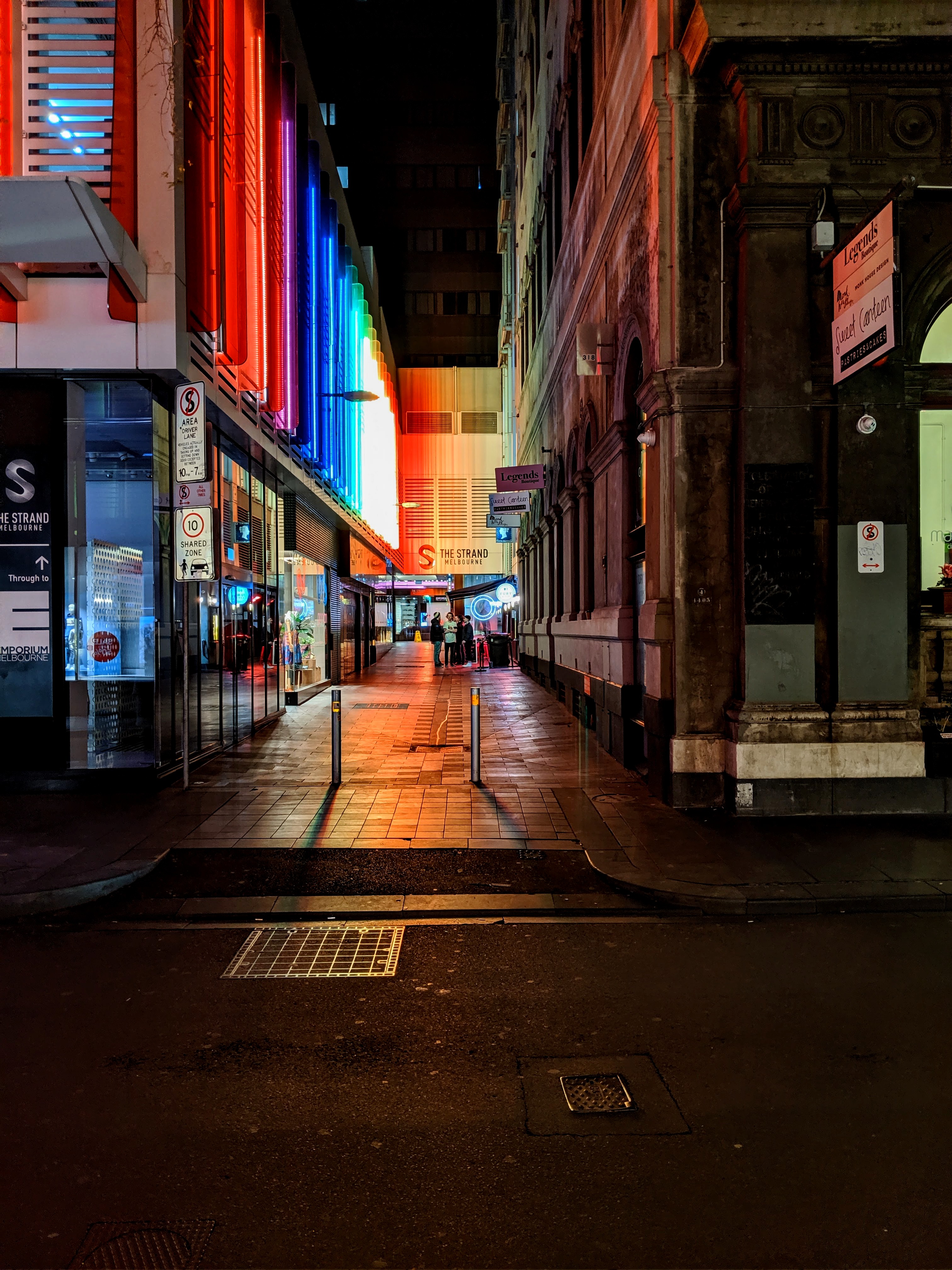 Eine Seitenstrasse, die tagsüber grau und unscheinbar ist, erstrahlt in Regenbogenfarben in der Nacht